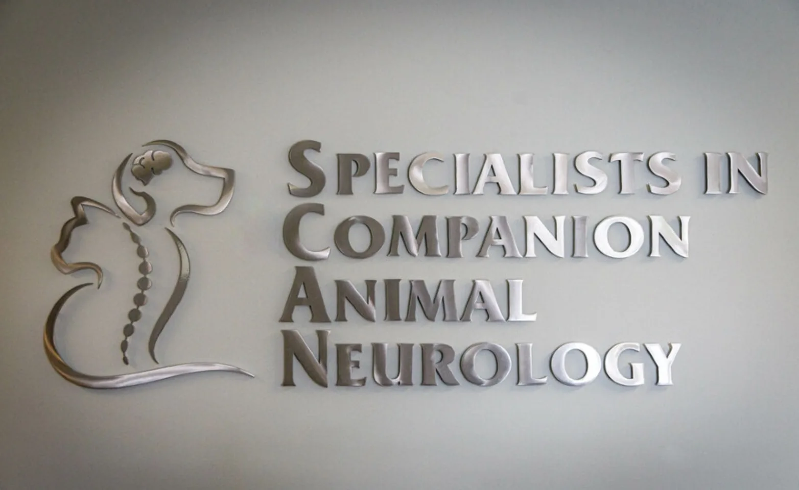 A metal cutout of the Specialists in Companion Animal Neurology (SCAN) logo hanging on a wall